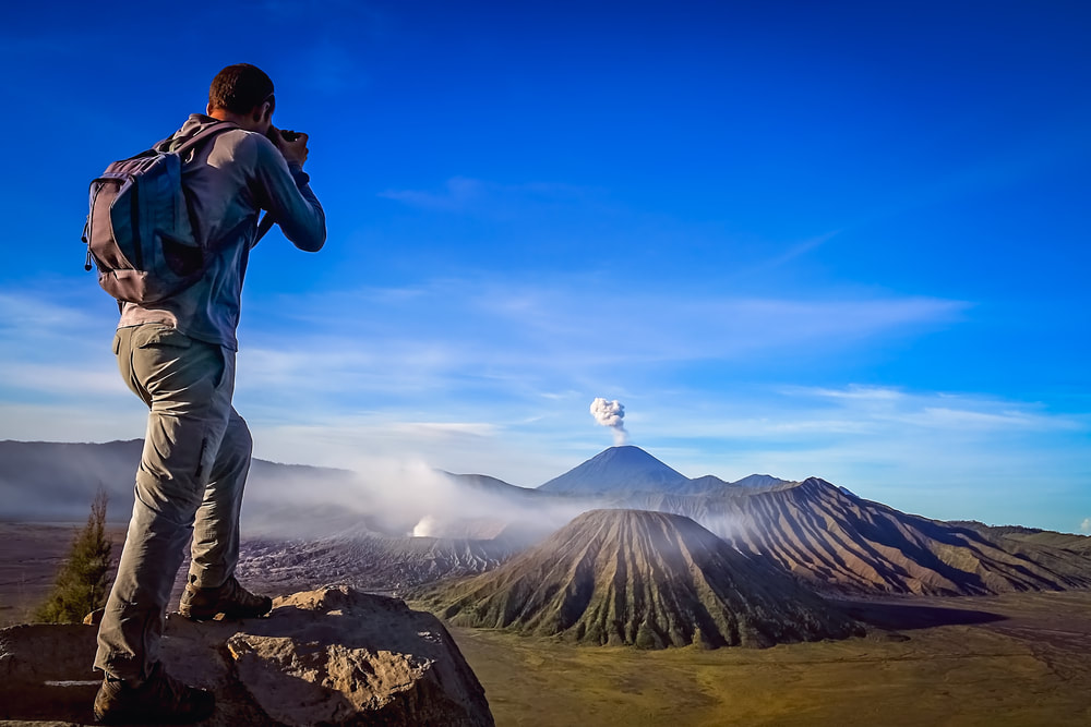 Tourist taking a ;picture of a volcano. 